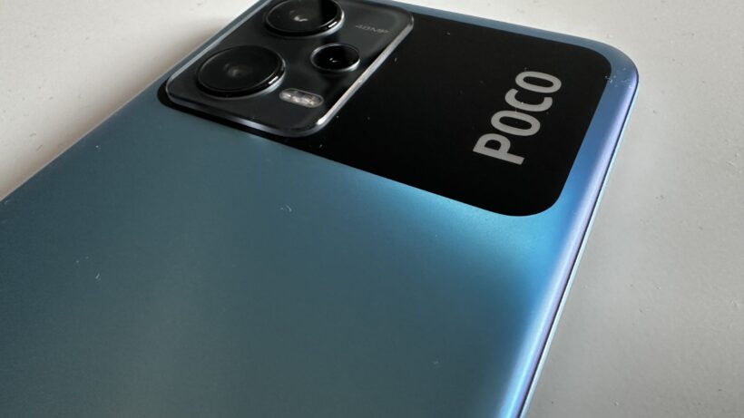 Крупный план камеры смартфона Poco X5 5G на текстурированной синей поверхности.