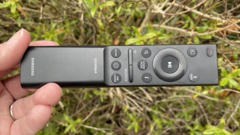 Пульт дистанционного управления для саундбара Samsung HW-Q990B. Рука, держащая пульт дистанционного управления для саундбара…