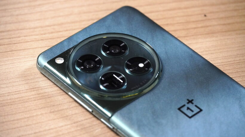 Выступ камеры OnePlus 12. Смартфон OnePlus с круглым модулем камеры на деревянной поверхности.