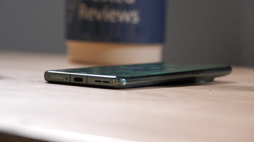 OnePlus 12 в профиль. Смартфон OnePlus 12 на деревянной поверхности с размытым фоном.
