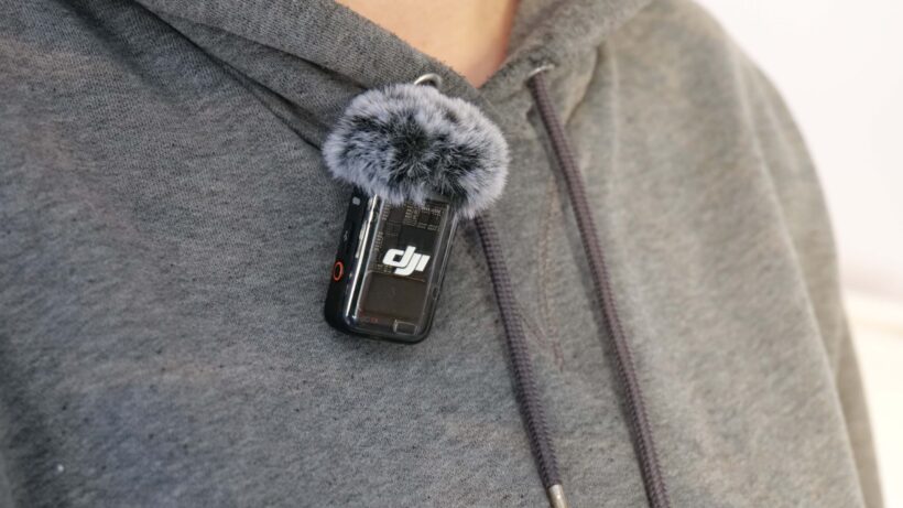 DJI Mic 2, прикрепленный к толстовке. DJI Mic 2, прикрепленный к серой толстовке человека с ветрозащитным экраном.