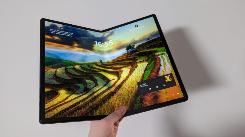 Lenovo ThinkPad X1 Fold в разложенном виде в руке. Рука, держащая Lenovo ThinkPad X1 Fold с обоями в альбомной ориентации.