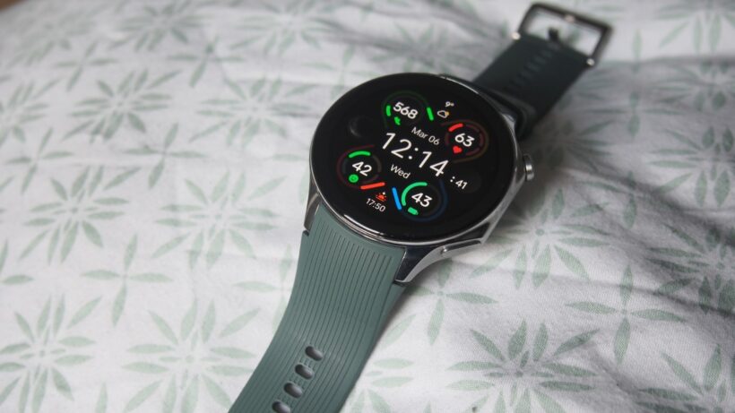 OnePlus Watch 2 на кровати. OnePlus Watch, отображающие время и статистику тренировок на ремешке.